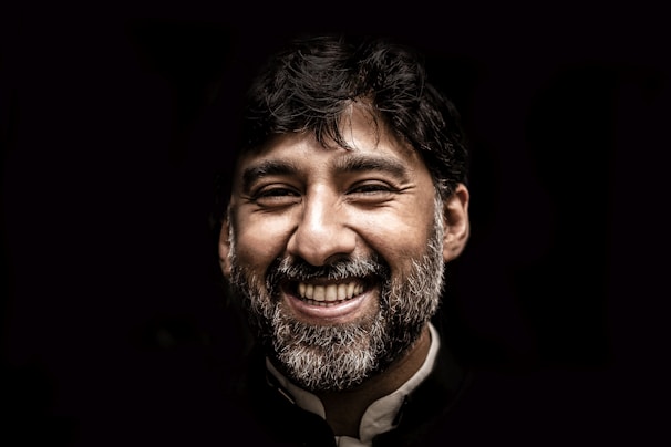 A confident man smiling warmly, set against a clean white background with soft blue and red color accents.