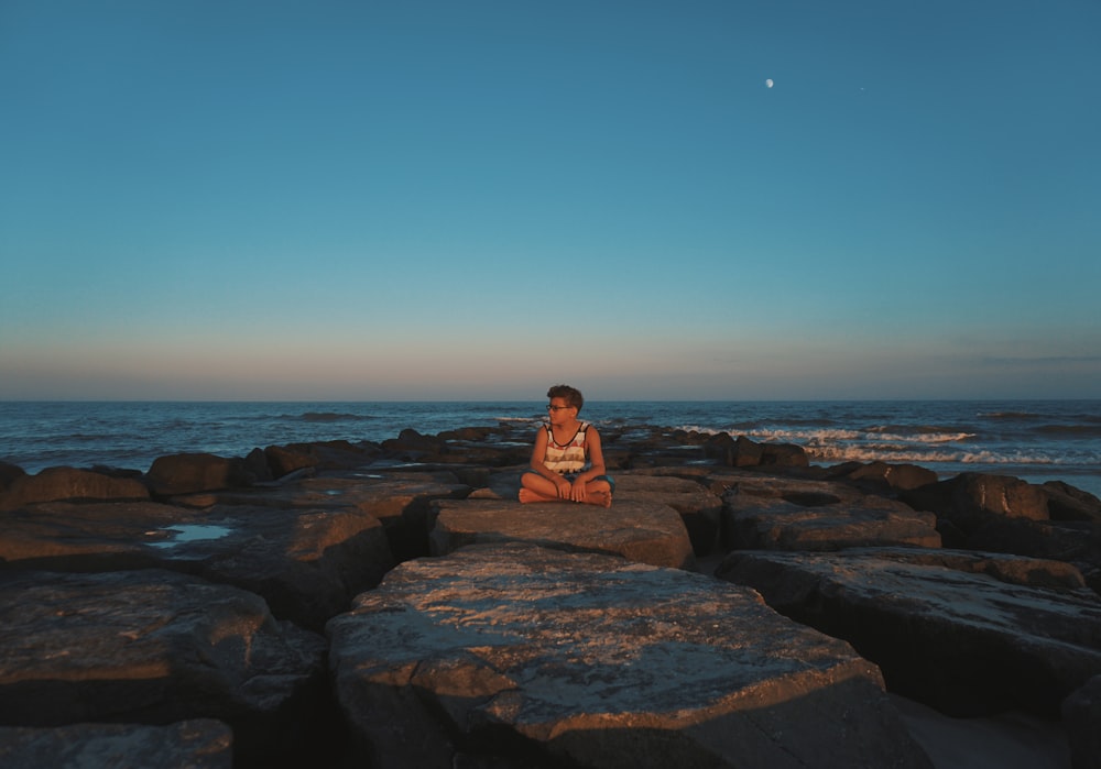 Une femme assise sur des rochers face à l’océan