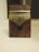 A wooden kalimba with a dark wood base and metal tines is centered against a soft, neutral background. The texture of the wood is smooth with visible grain patterns, and the metal tines are arranged in a fan-like pattern.