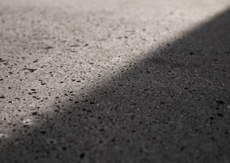 A textured concrete surface with shadows casting a diagonal line across it, highlighting the roughness and small pits in the material.