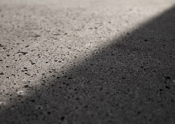 A textured concrete surface with shadows casting a diagonal line across it, highlighting the roughness and small pits in the material.