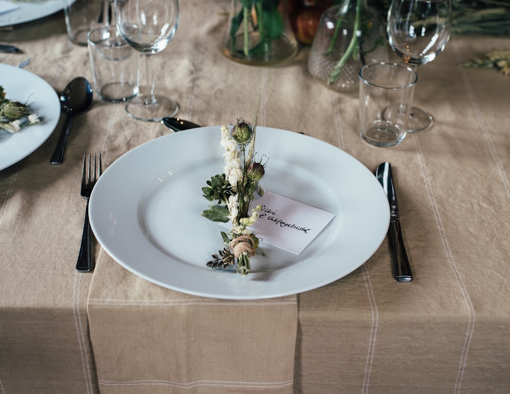 흰색 접시에 녹색과 흰색 장식 꽃과 테이블 위에 놓인 수저