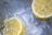 Two slices of lemon floating in water with visible ripples and bubbles. The slices are of a bright yellow color with white rinds. Water appears to be moving, causing the lemons to drift apart.