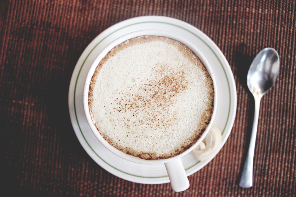 top view photo of white ceramic mug on saucer beside siver tablespoon