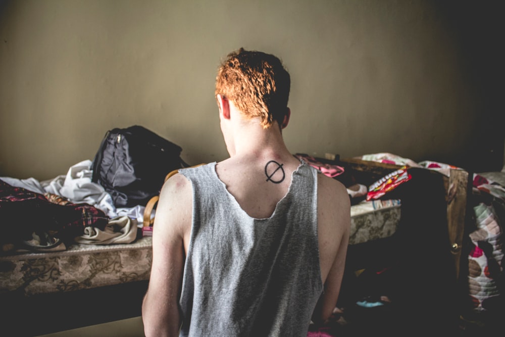 A young man in a tank top standing next to a bunk bed with a backpack on top of it