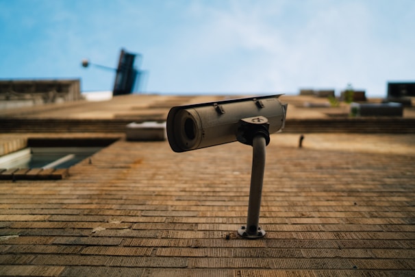 Close-up of a CCTV camera mounted on a building corner under a bright blue sky.