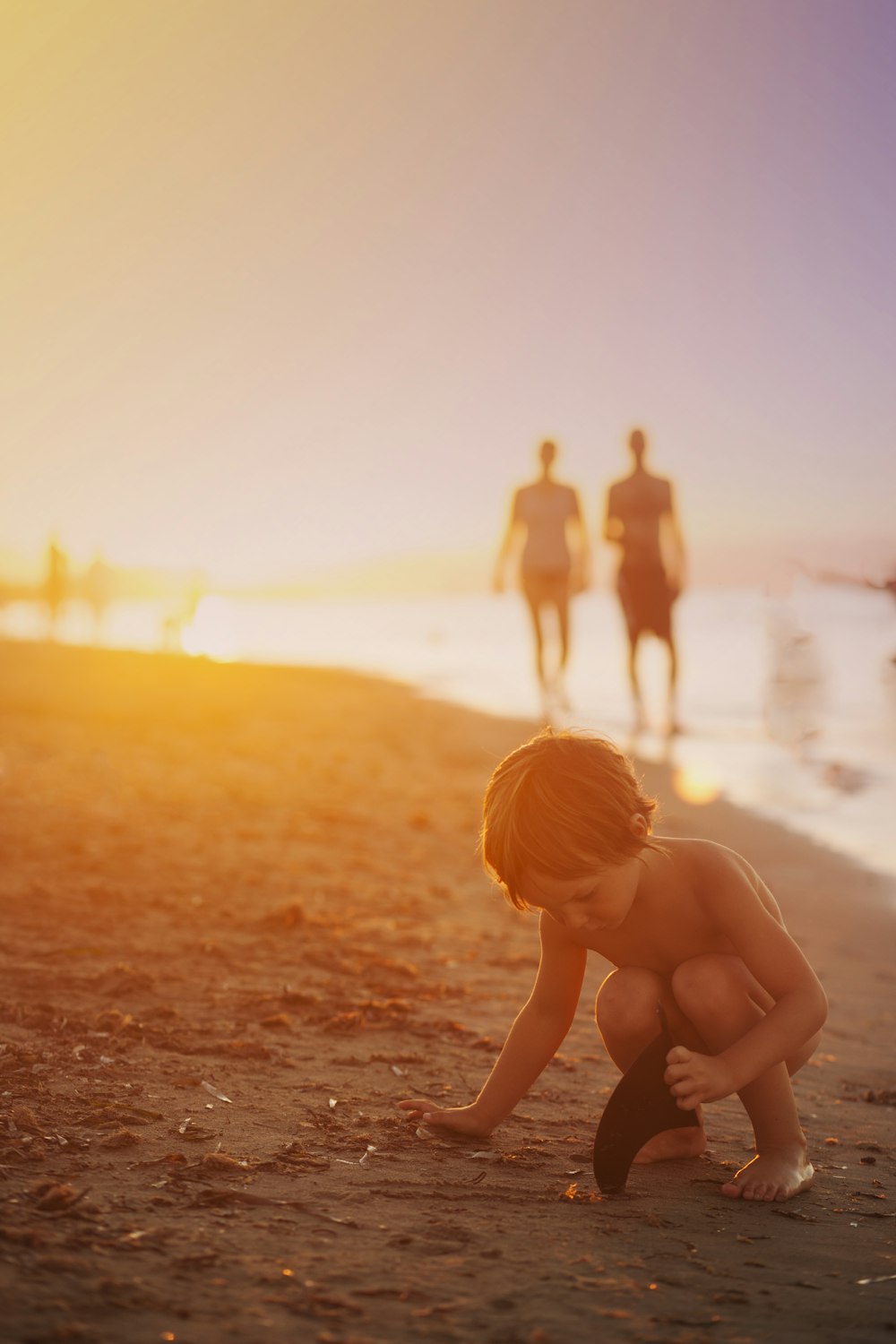 Niño jugando arena en la orilla del mar durante la puesta del sol