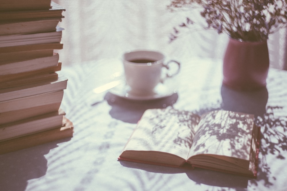 Libro abierto junto a una taza de té de cerámica blanca en un platillo