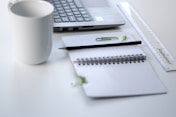 black pencil on ruled notepad beside white ceramic mug and gray laptop computer