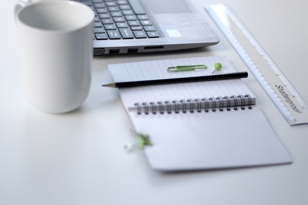 A notepad, a ruler, a mug and a laptop on a white desk