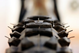 A close-up view of a rugged bicycle or motorcycle tire, showcasing its deep treads and texture. The background is slightly blurred, drawing attention to the details of the tire.