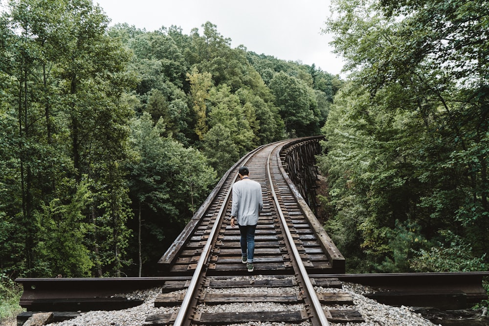 man standing on railway surrounded by trees