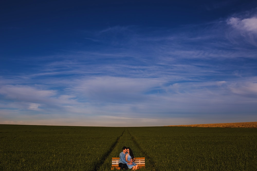 photo of two man and woman sitting on bench on grass field