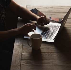 gray laptop computer on brown wooden table beside person sitting on chair