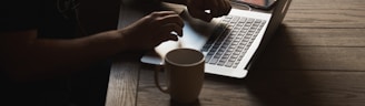 gray laptop computer on brown wooden table beside person sitting on chair