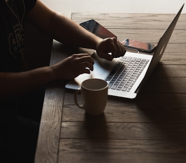 gray laptop computer on brown wooden table beside person sitting on chair