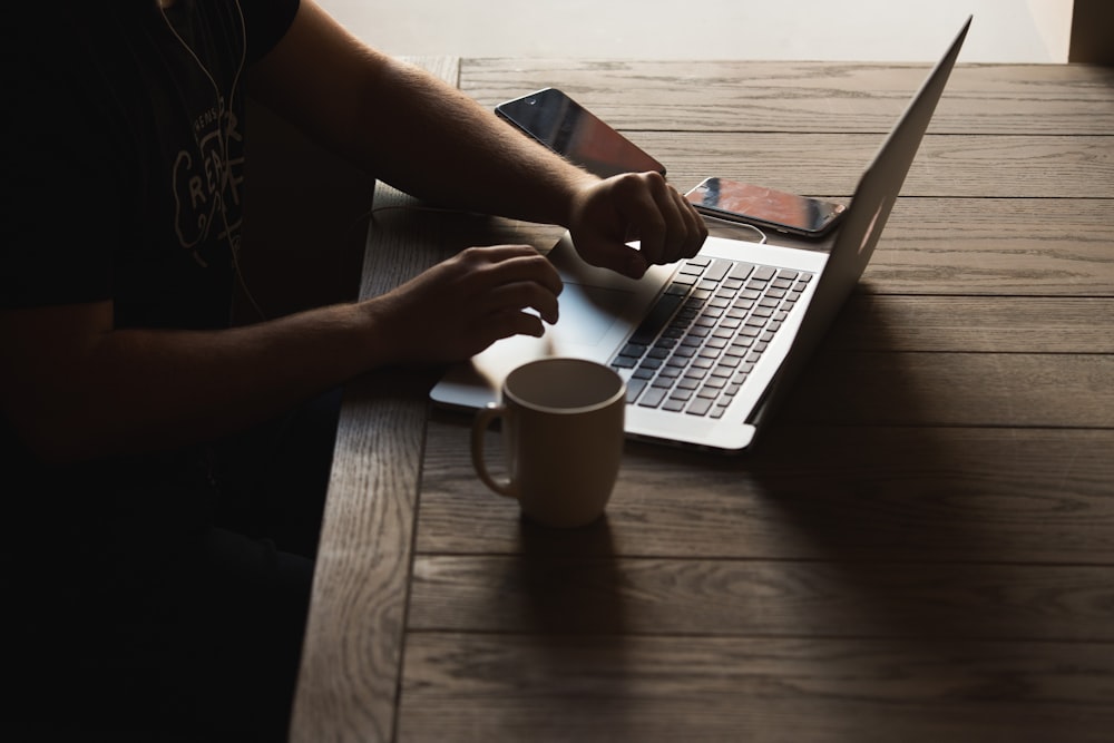 gray laptop computer on brown wooden table beside person sitting on chair