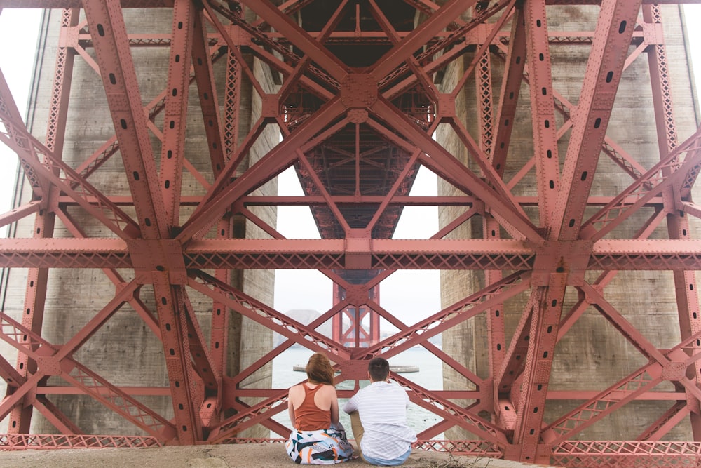 man and woman sitting near red metal scaffolding during daytime