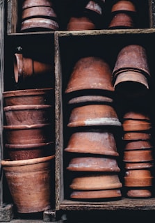 Numerous terracotta pots are neatly stacked in wooden compartments. The pots vary in size and are made of weathered, reddish-brown clay, with some showing signs of wear and aging.