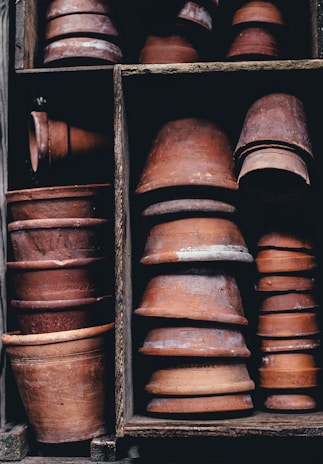 Numerous terracotta pots are neatly stacked in wooden compartments. The pots vary in size and are made of weathered, reddish-brown clay, with some showing signs of wear and aging.