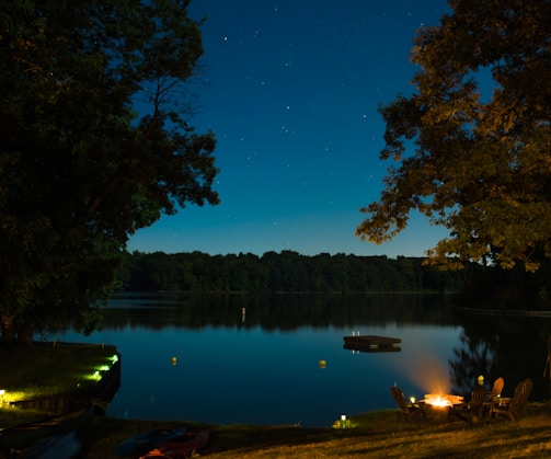 A cozy campfire glowing under a star-filled sky beside a quiet lake.