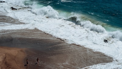 two person on seashore facing ocean waves wafe teams background