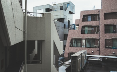 Concrete and brick buildings with geometric shapes form an urban landscape. Several windows, balconies, and air conditioning units are visible. The architecture is modern and somewhat industrial.