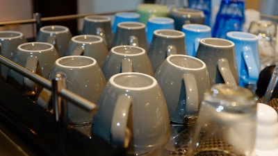 A row of freshly glazed ceramic mugs drying on a wooden shelf.