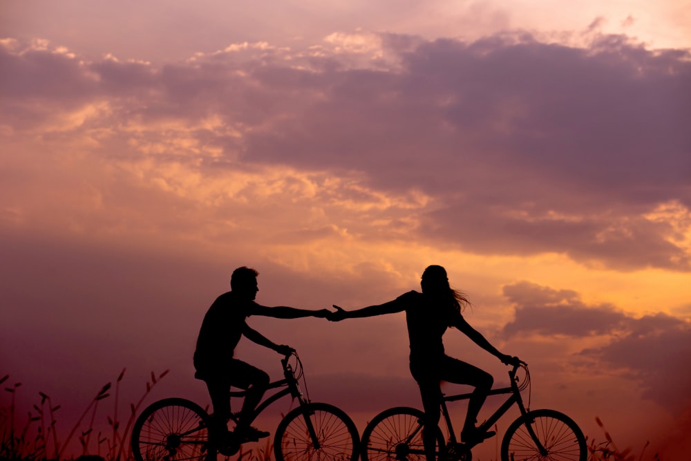 Frau auf dem Fahrrad greift nach der Hand des Mannes hinter sich, auch auf dem Fahrrad