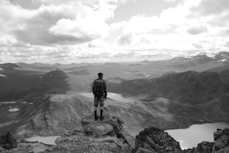 A scenic view of a traveler standing on a mountain peak overlooking a vast landscape.