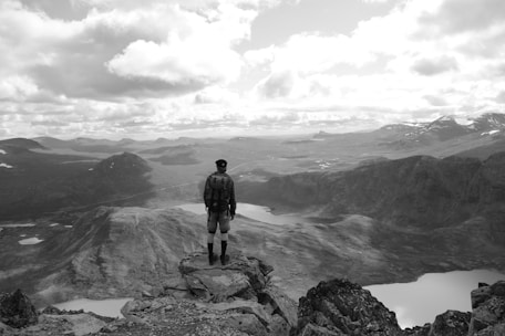 A scenic view of a traveler standing on a mountain peak overlooking a vast landscape.