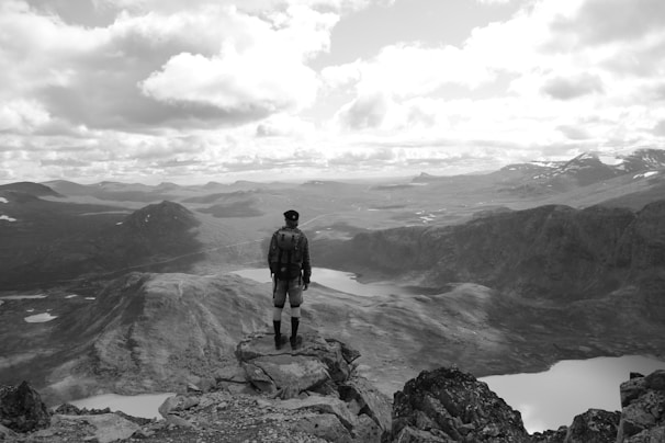 A scenic view of a traveler standing on a mountain peak overlooking a vast landscape.