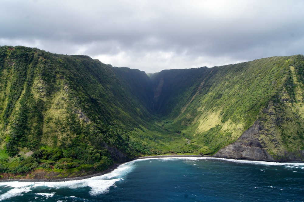 montaña densa verde al lado del cuerpo de agua bajo el cielo nublado blanco durante el día