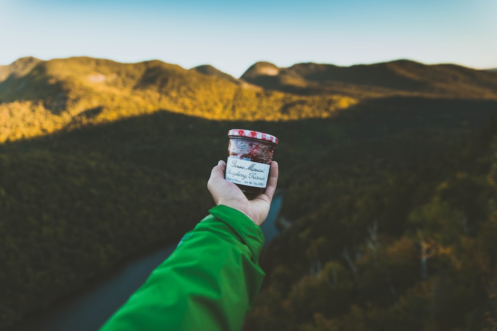 person holding clear glass jar with cap near mountain