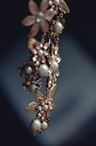 An elegant piece of jewelry featuring floral designs with intricate metalwork and adorned with pearls and gemstones. The craftsmanship is delicate, with attention to detail in the arrangement of the flower petals and leaves.