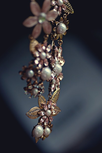 An elegant piece of jewelry featuring floral designs with intricate metalwork and adorned with pearls and gemstones. The craftsmanship is delicate, with attention to detail in the arrangement of the flower petals and leaves.