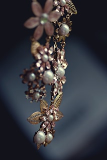 An elegant piece of jewelry featuring floral designs with intricate metalwork and adorned with pearls and gemstones. The craftsmanship is delicate, with attention to detail in the arrangement of the flower petals and leaves.