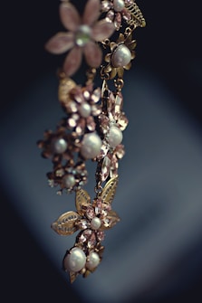 An elegant piece of jewelry featuring floral designs with intricate metalwork and adorned with pearls and gemstones. The craftsmanship is delicate, with attention to detail in the arrangement of the flower petals and leaves.