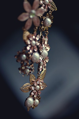 An elegant piece of jewelry featuring floral designs with intricate metalwork and adorned with pearls and gemstones. The craftsmanship is delicate, with attention to detail in the arrangement of the flower petals and leaves.