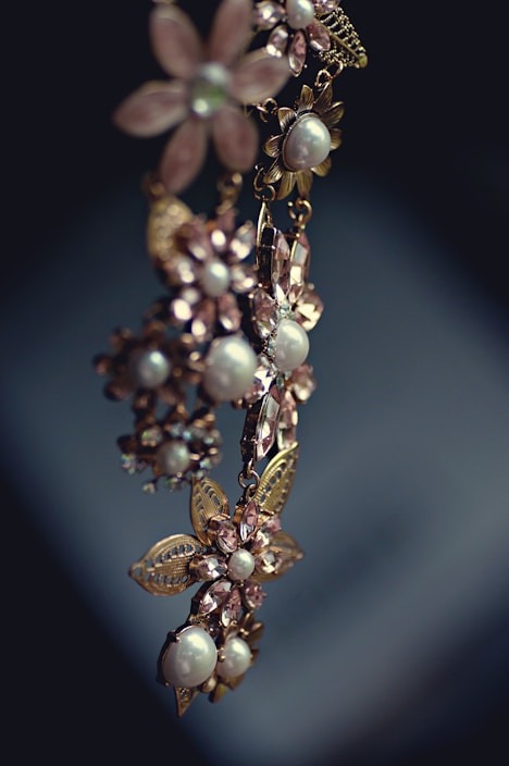 An elegant piece of jewelry featuring floral designs with intricate metalwork and adorned with pearls and gemstones. The craftsmanship is delicate, with attention to detail in the arrangement of the flower petals and leaves.