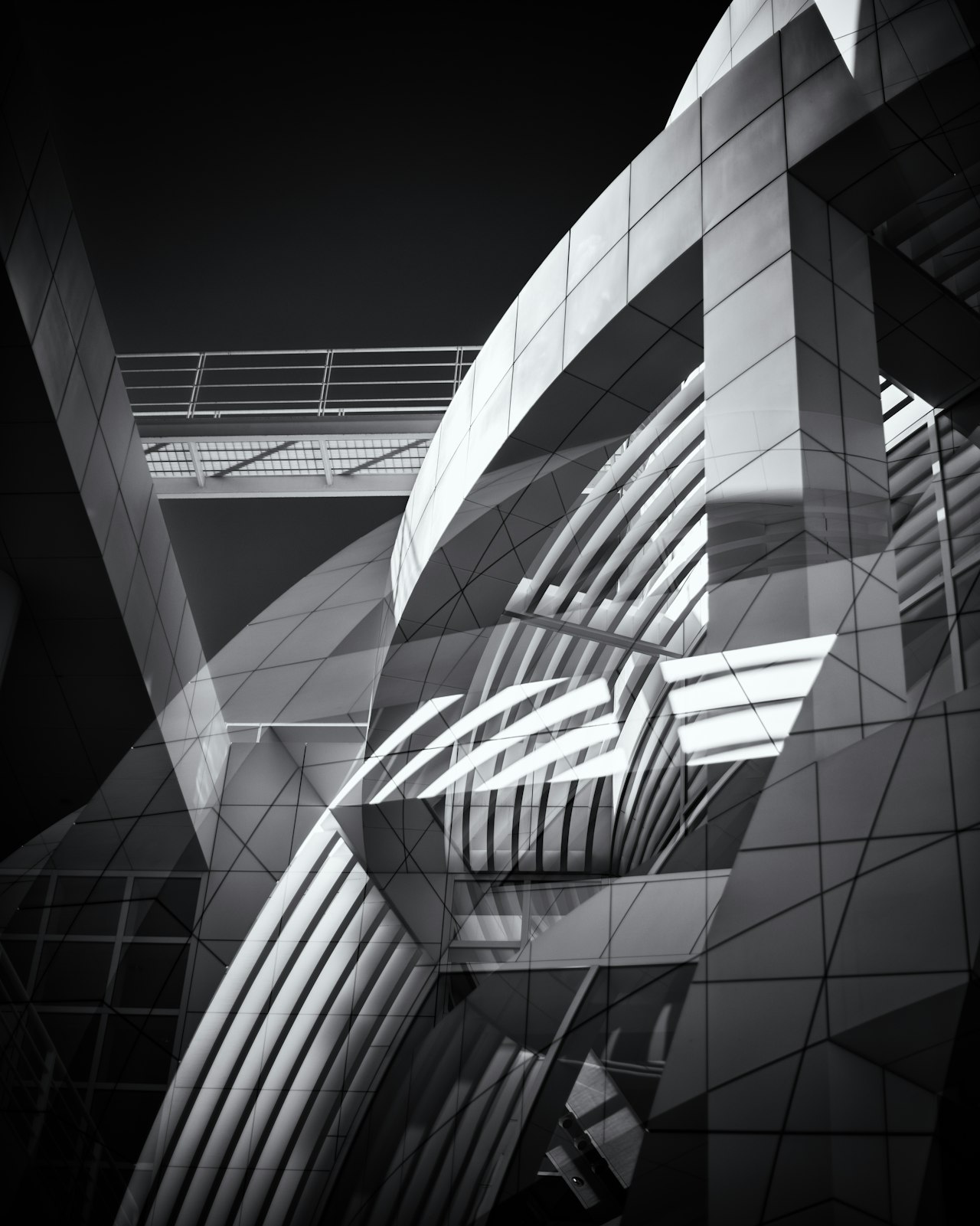 Modern building exterior with sweeping curved cladding and a glass-and-steel bridge.