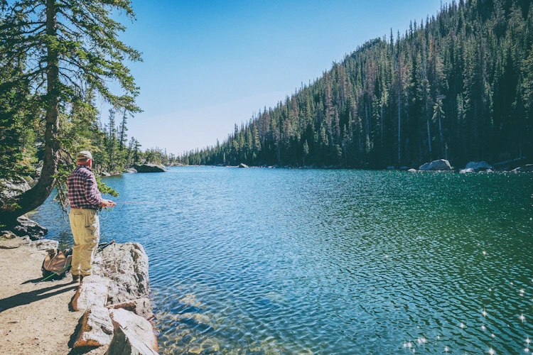 Fisherman sitting on a rock at an alpine lake surrounded by Colorado pine forest at Emerald Lake