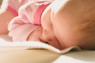 A close-up of a sleeping baby wearing a pink outfit, resting peacefully on a soft surface with warm lighting enhancing the serene atmosphere.