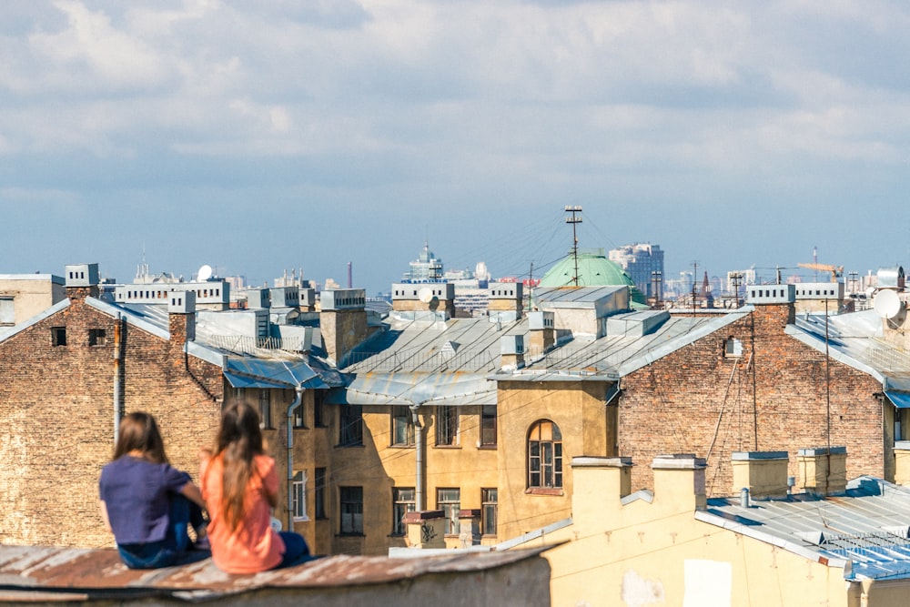 two women sitting on roof overlooking building during daytime