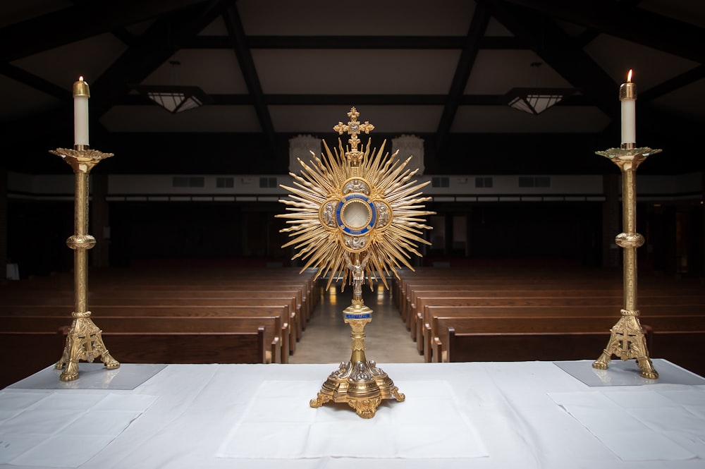 Gold colored religious objects and candles on a table at the front of a church aisle.