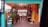 An artistic space with bright colors and decorative lighting. The entrance is framed with a teal and orange color scheme, and the area is adorned with potted plants and various artistic signs. A colorful trash can and a welcoming sign are visible, suggesting a cozy and creative environment.