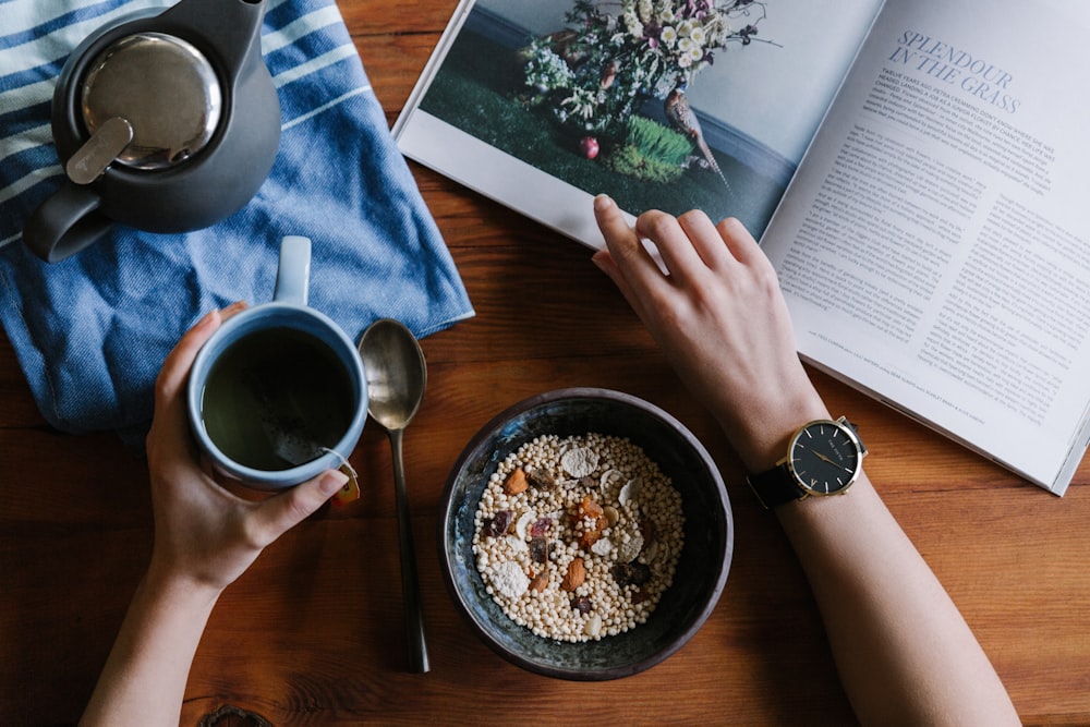 person holding blue ceramic mug and white magazine