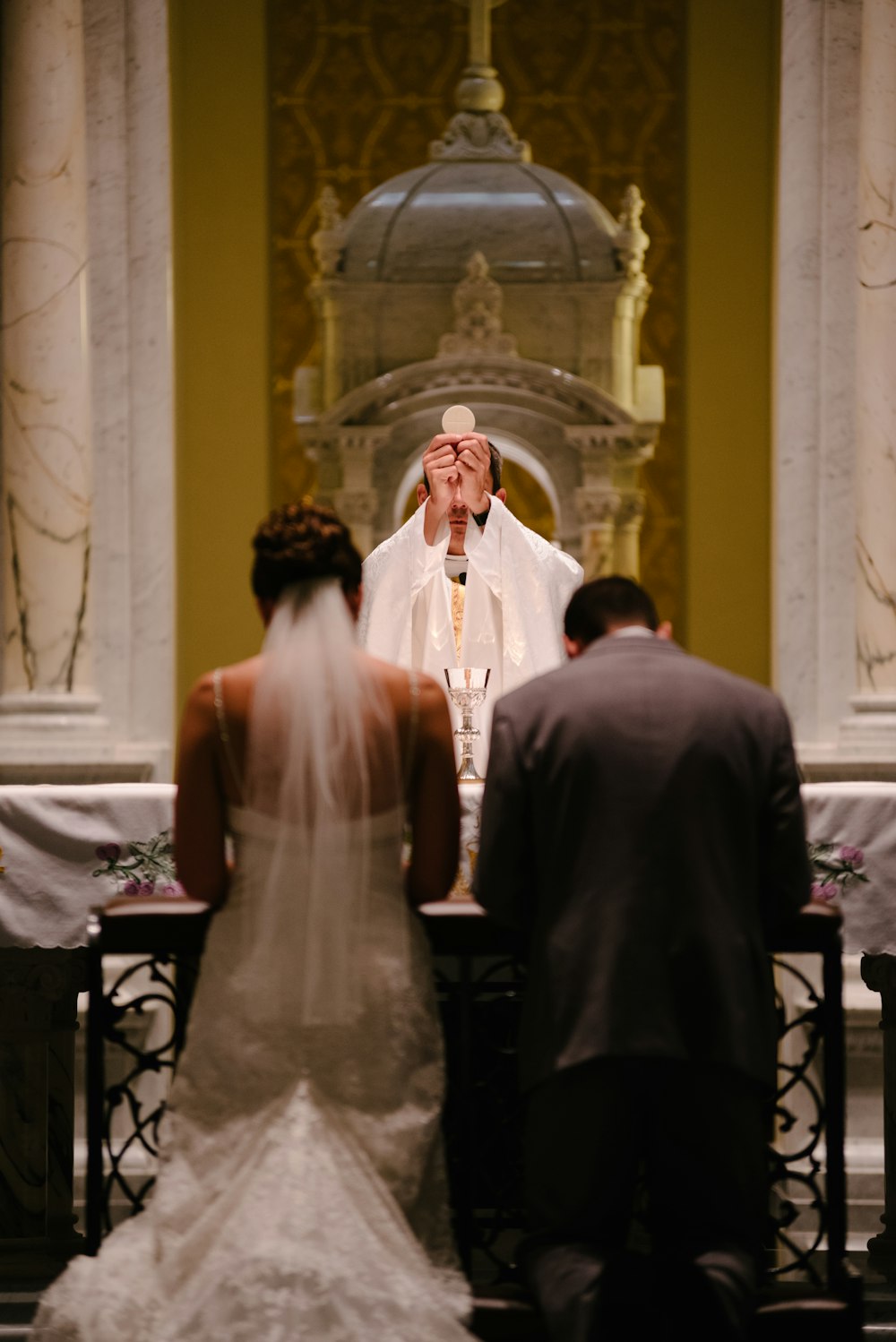 Bräutigam und Braut knien vor Priester und erheben das Heilige Sakrament