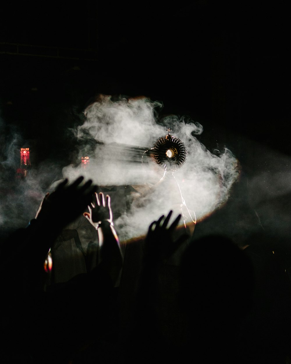 A religious object held up in front of a fog machine, with a crowd raising their hands.