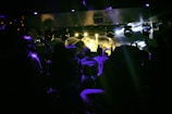 Wide shot of a dimly lit venue filled with dancing fans and pulsating visuals.